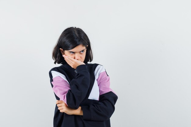 Klein meisje in shirt met hand op mond en op zoek triest, vooraanzicht.