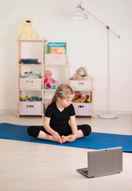 Klein meisje in sportkleding die online video op laptop bekijkt en workout- of fitnessoefeningen doet