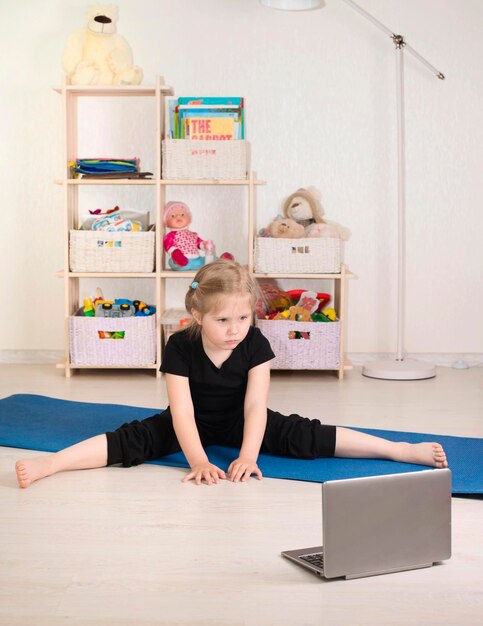 Klein meisje in sportkleding die online video op laptop bekijkt en workout- of fitnessoefeningen doet