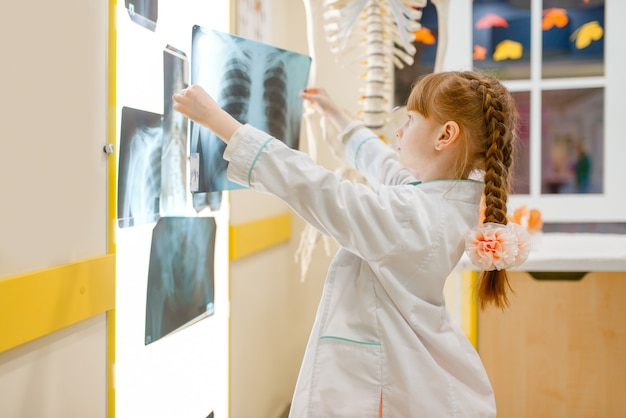 Klein meisje in uniform kijkt naar de x-ray, dokter