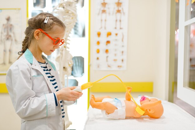 Klein meisje in uniform spelen arts met pop