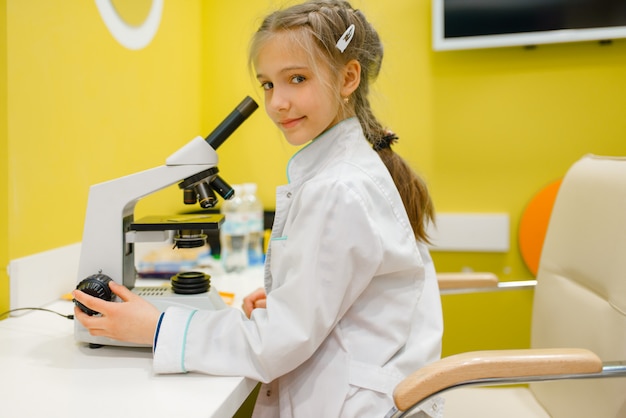 Klein meisje in uniform zit op de Microscoop en arts spelen