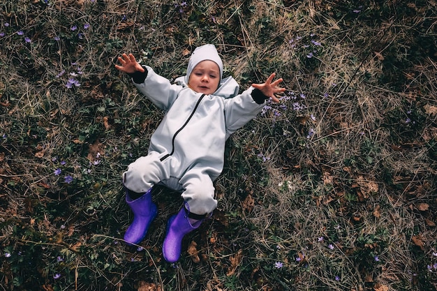 Klein meisje in violette laarzen en blauwe overall ligt in het lente bloeiende bos