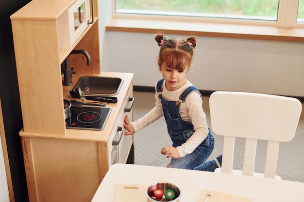 Klein meisje in vrijetijdskleding heeft plezier door met speelgoed in de keuken te spelen