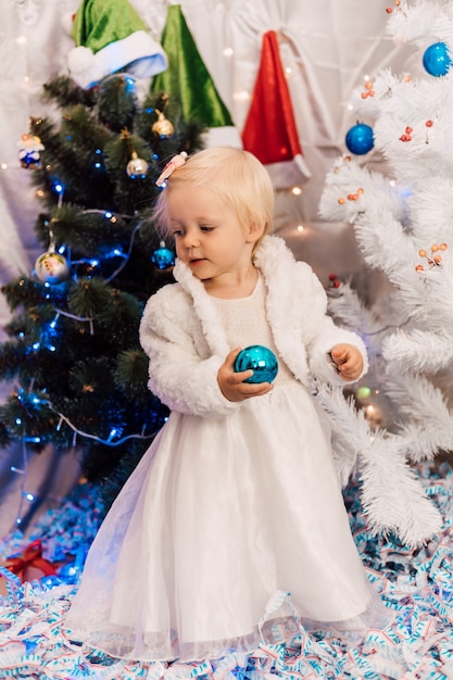 Klein meisje in witte jurk speelt bij de kerstboom