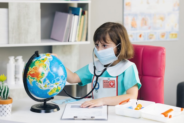 Klein meisje is gekleed in medische kleding met een stethoscoop in haar handen onderzoekt en speelt een spel om de planeet aarde te genezen.