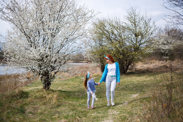 Klein meisje kind en moeder vrouw loopt door het bos van de lente met bloeiende bomen, het begin van de lente, familievakantie