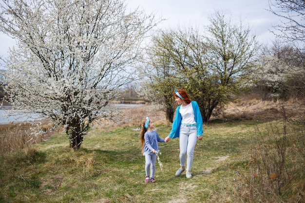 Klein meisje kind en moeder vrouw loopt door het bos van de lente met bloeiende bomen, het begin van de lente, familievakantie