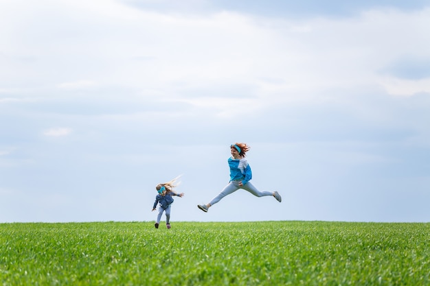 Klein meisje kind en moeder vrouw rennen en springen, groen gras in het veld, zonnig lenteweer, glimlach en vreugde van het kind, blauwe lucht met wolken