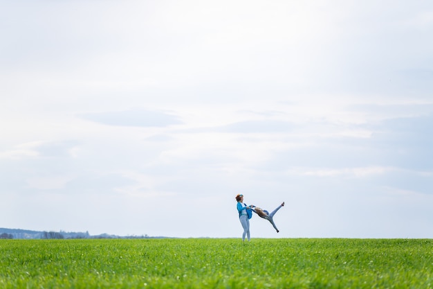 Klein meisje kind en moeder vrouw rennen en springen, groen gras in het veld, zonnig lenteweer, glimlach en vreugde van het kind, blauwe lucht met wolken