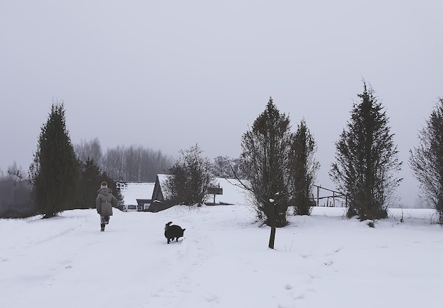 Klein meisje kind in een beige jas lopen met kleine zwarte hond op besneeuwde veld in het dorp.