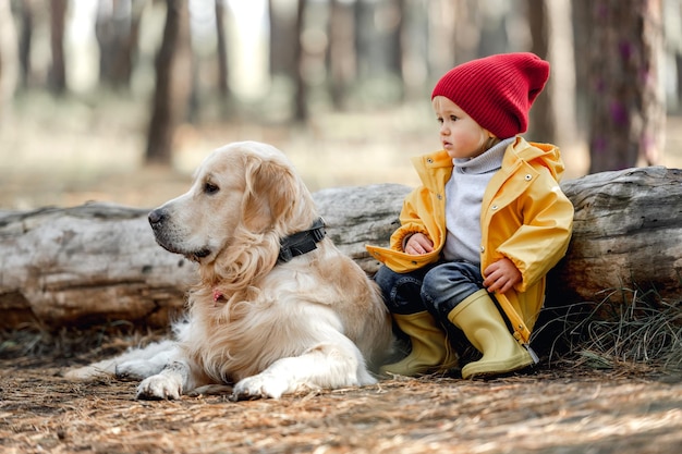 Klein meisje kind met golden retriever hond zittend op de grond dicht bij log en terugkijkend in herfst bos Vrouwelijke jongen en hondje huisdier portret in de natuur