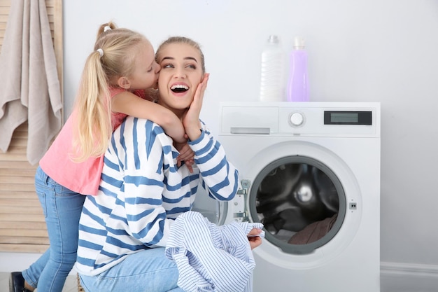 Klein meisje knuffelt haar moeder terwijl ze thuis de was doet