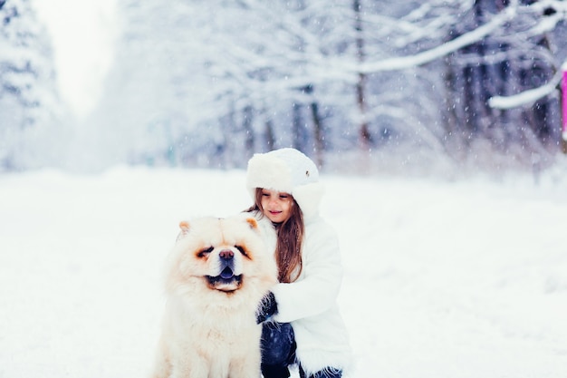 Klein meisje knuffelt schattige hond chow chow in winterbos