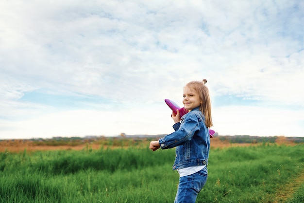 Klein meisje, lanceert een speelgoedvliegtuig, in de lucht. child lanceert een speelgoedvliegtuig. mooi meisje, staat op het gras en lanceert een roze speelgoedvliegtuig