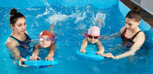 Klein meisje leert zwemmen in binnenzwembad met poolplank en trainer