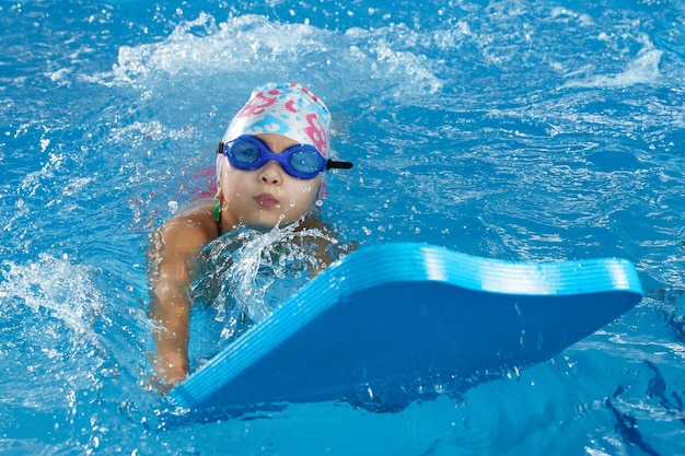 Klein meisje leert zwemmen in binnenzwembad met poolplank