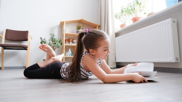 Klein meisje liggend op een houten vloer met een boek