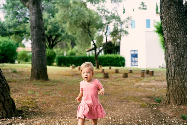 Klein meisje loopt met haar mond open op een open plek bij de boomstronken in de tuin