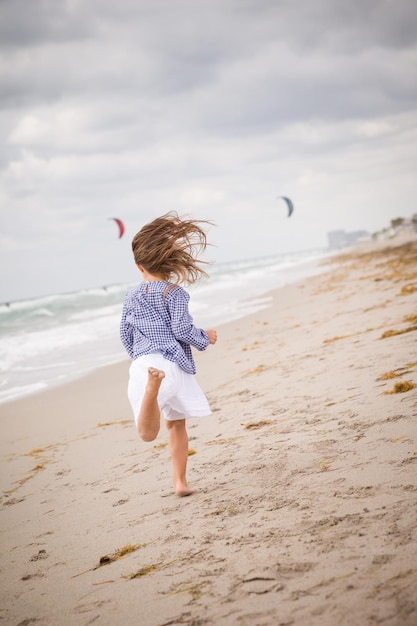 Klein meisje loopt op het strand van de oceaan op een bewolkte dag vakantie aan zee wind in het haar