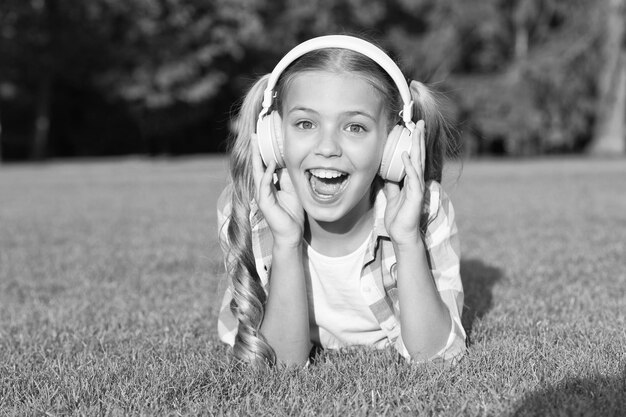 Klein meisje luister audioboek nieuwe technologie voor kinderen gelukkige jeugdherinneringen luisteren naar muziek terug naar school kind studeren in park ontspannen op groen gras in koptelefoon Hooked On Learning