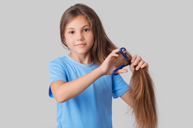 Klein meisje met appelwangetjes in een blauw t-shirt dat haar lange haar gaat afknippen