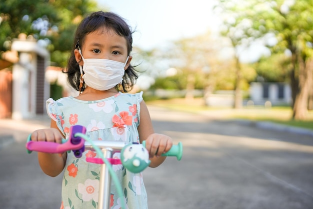 Klein meisje met beschermend gezichtsmasker buiten scooter spelen