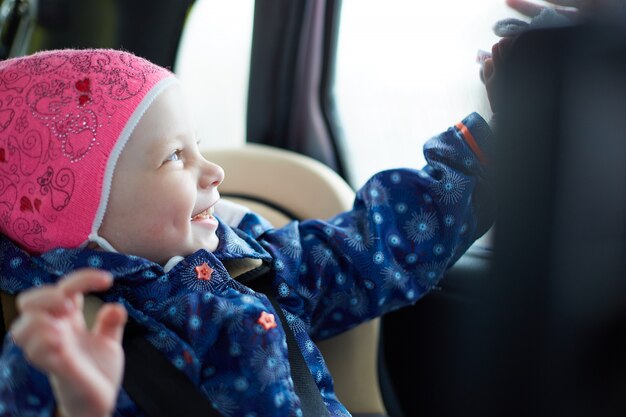 klein meisje met blauwe ogen zitten in een kinderzitje op de achterbank van de auto bij het raam