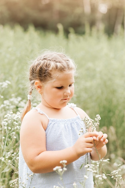 Klein meisje met bloemen loopt in de zomer in een bloemenveld