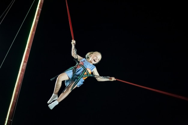 Klein meisje met blond haar in de lucht op de katapultrit tegen de zwarte lucht. Leuke zomervakantie.