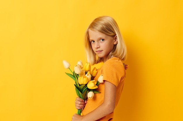 Klein meisje met blond haar met een boeket gele bloemen op een gele achtergrond