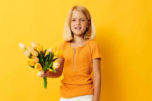 Klein meisje met blond haar met een boeket gele bloemen op een gele achtergrond
