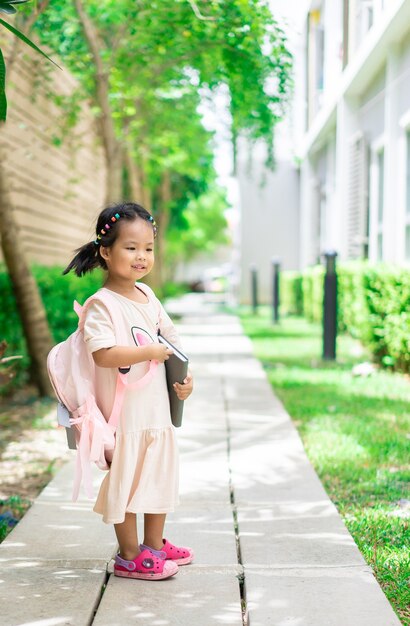 klein meisje met boek en rugzak wandelen in het park klaar terug naar school