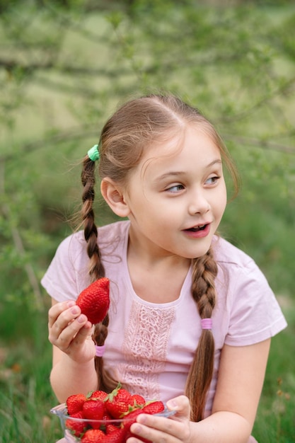Klein meisje met bord met aardbeien in de natuur Tuinieren en landbouwconcept Veganistisch vegetarisch Verticaal