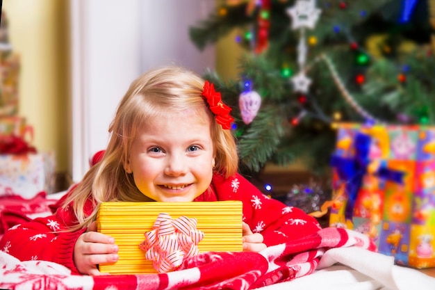 Klein meisje met cadeau onder de kerstboom Gelukkig nieuwjaarsconcept