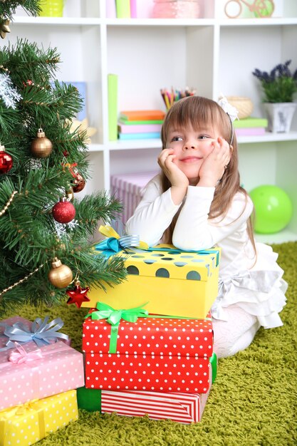 Klein meisje met cadeautjes bij de kerstboom in de kamer