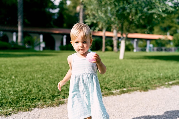 Klein meisje met een bal in haar hand loopt langs het grindpad in het park