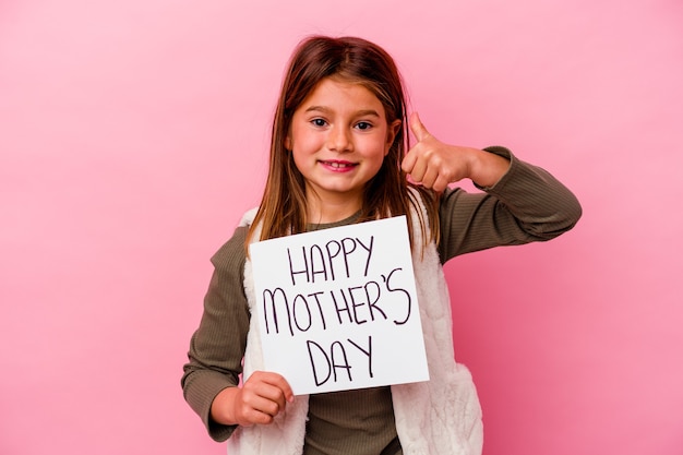 Klein meisje met een banner voor gelukkige moeders dag geïsoleerd op roze achtergrond