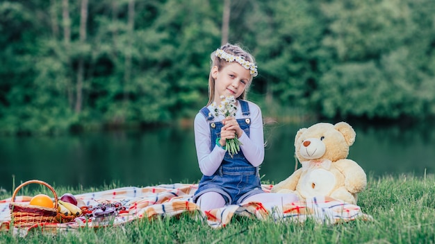 Klein meisje met een boeket madeliefjes zittend op het gazon op een zomerdag.