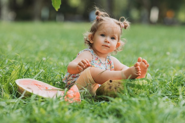 klein meisje met een grappig kapsel eet een watermeloen op het gazon in het park gezonde snack voor kinderen