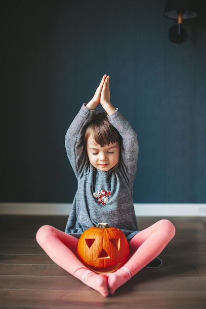 Klein meisje met een Halloween-pompoen zittend in een lotushouding