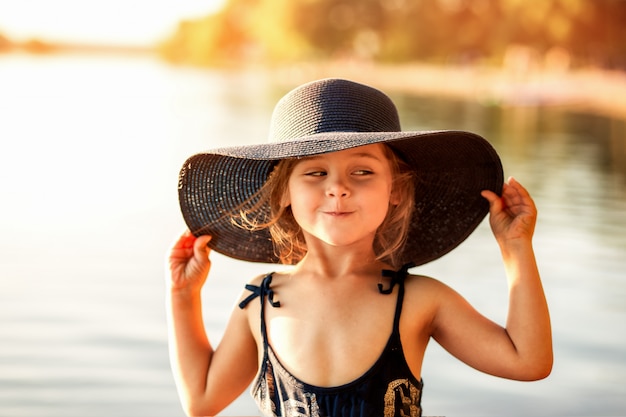 klein meisje met een hoed aan de rivier in de zomer