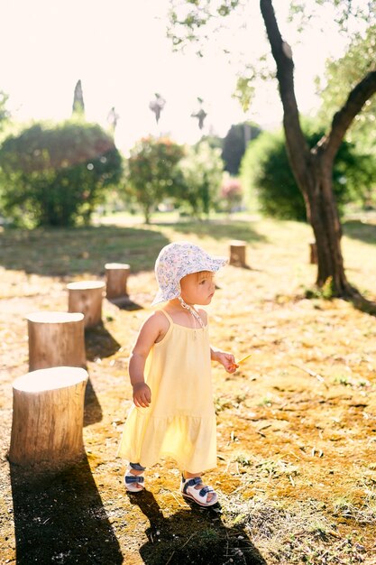 Klein meisje met een hoed loopt in het park met een stok in haar handen