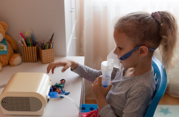 Klein meisje met een inhalatormasker aan tafel Griepseizoen