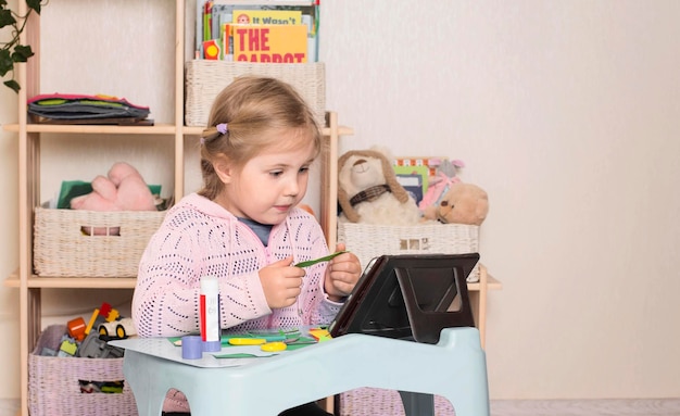 Klein meisje met een schaar en lijm Portret van een klein schattig meisje dat een papier snijdt met tablet pc