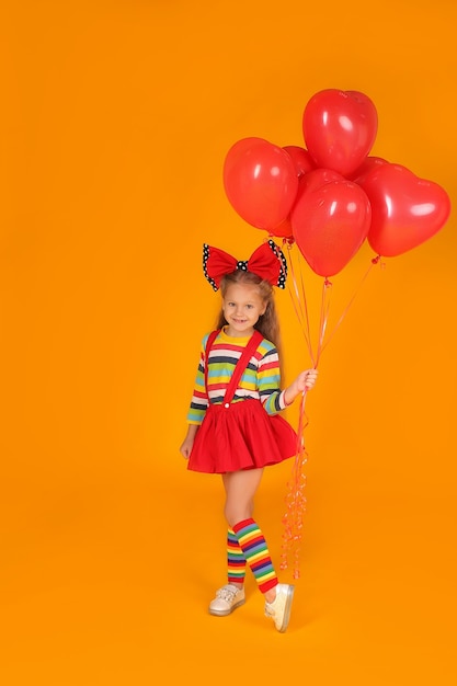 Klein meisje met een strik op haar hoofd in een gekleurd t-shirt in een rode rok houdt ballonnen in haar handen