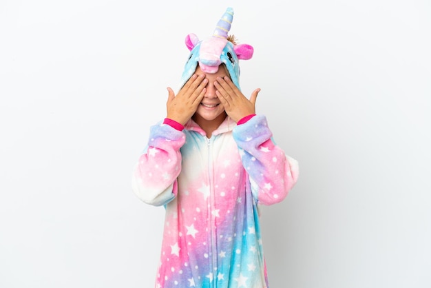 Klein meisje met eenhoorn pyjama geïsoleerd op een witte achtergrond die ogen bedekt door handen