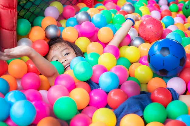 Foto klein meisje met gekleurde plastic ballen. grappig kind plezier binnenshuis.