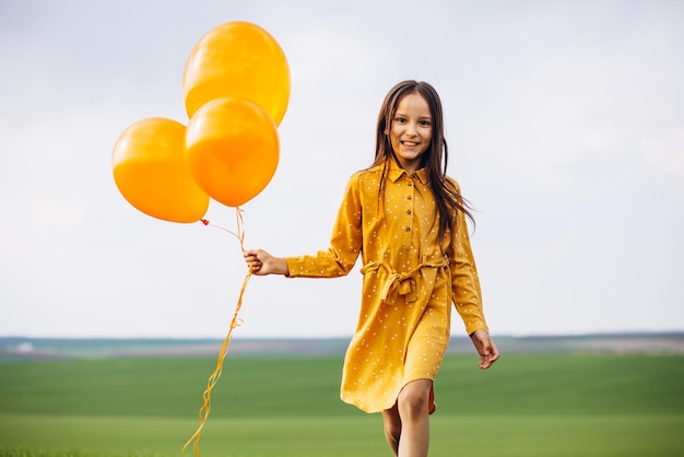 Klein meisje met gele ballonnen in het veld