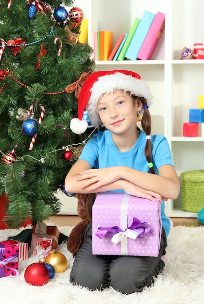 Klein meisje met geschenkdoos in de buurt van kerstboom